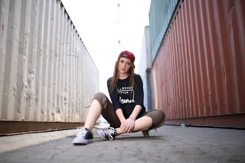 Free Woman Sitting on a Skateboard Near Shipping Containers Stock Photo