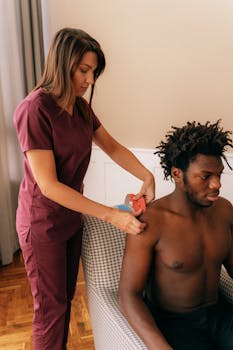 A physiotherapist uses kinesiology tape to treat an athlete's shoulder indoors.