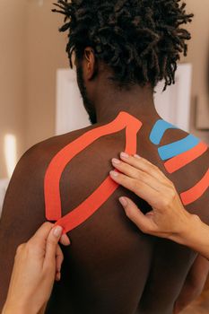 Close up of kinesio tape application on a man's shoulder for pain relief therapy. — photo by Antoni Shkraba Studio