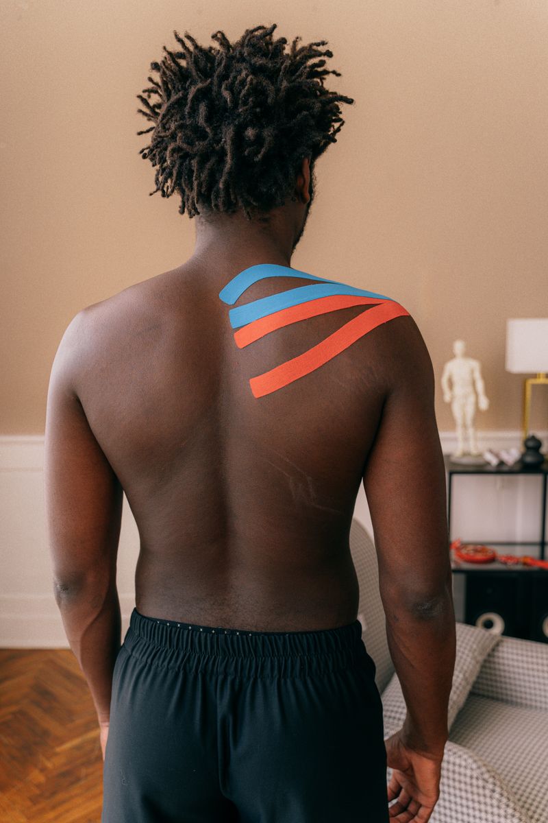 Back view of a male athlete with kinesiology tapes applied to the shoulder indoors