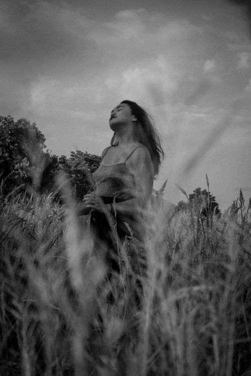 Free A graceful woman poses in a meadow, captured in moody black and white photography. Stock Photo