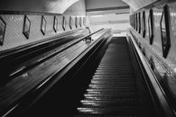 Black and white of from below of stairway with railings inside modern building with tiled walls decorated with pictures in black frames