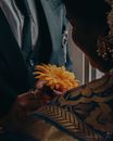 Crop anonymous son in formal suit giving blossoming flower to ethnic mom in ornamental apparel during festive event