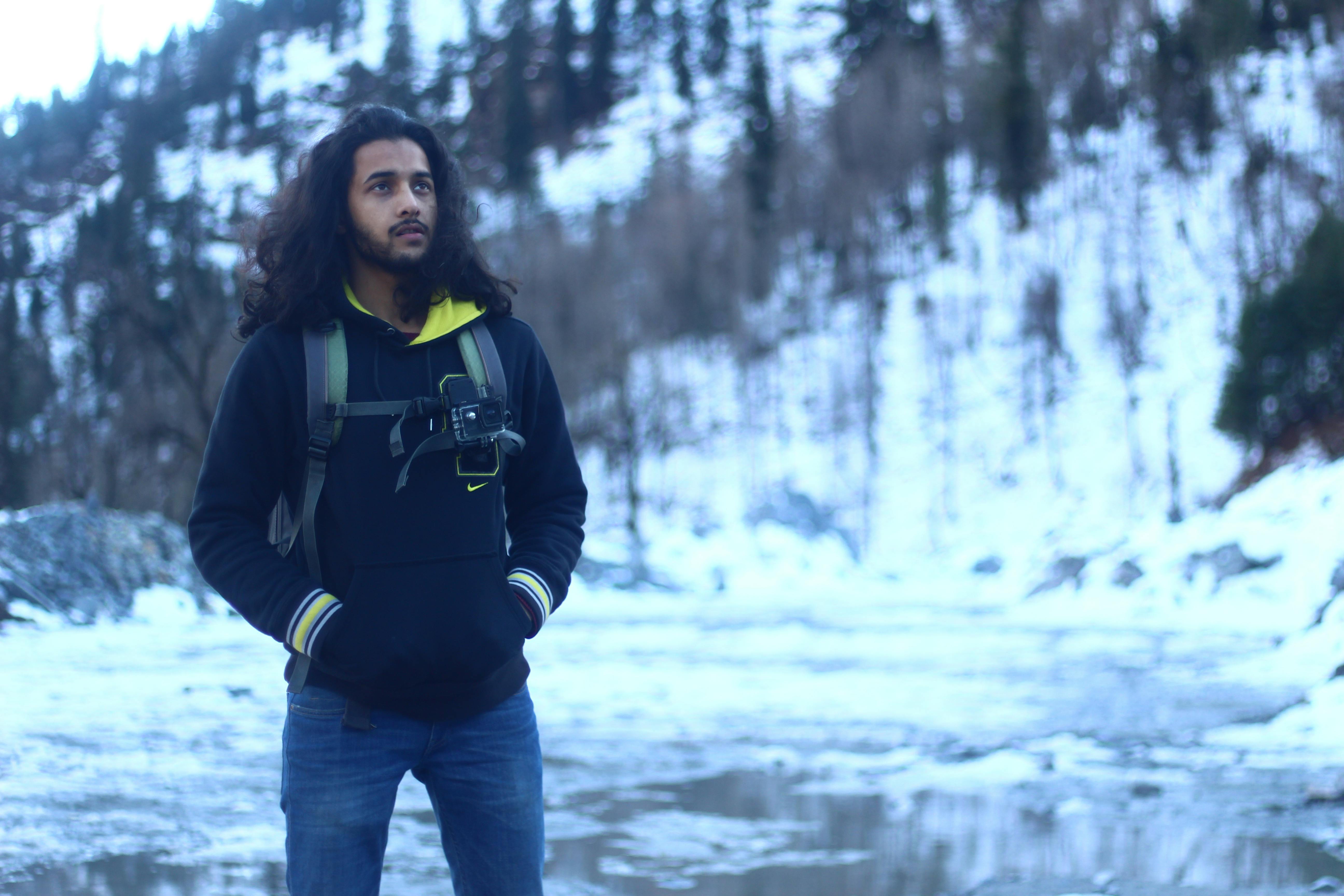 A young man with long hair and a backpack enjoying a snowy mountain adventure.
