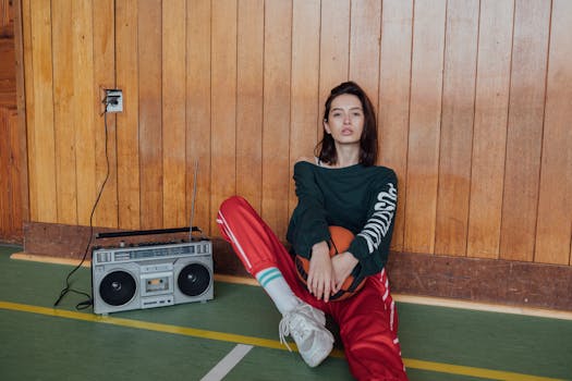 Stylish young woman in retro fashion sitting with a basketball and cassette player indoors.