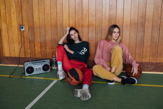 Two women sit casually indoors with basketballs, exuding a relaxed vibe.