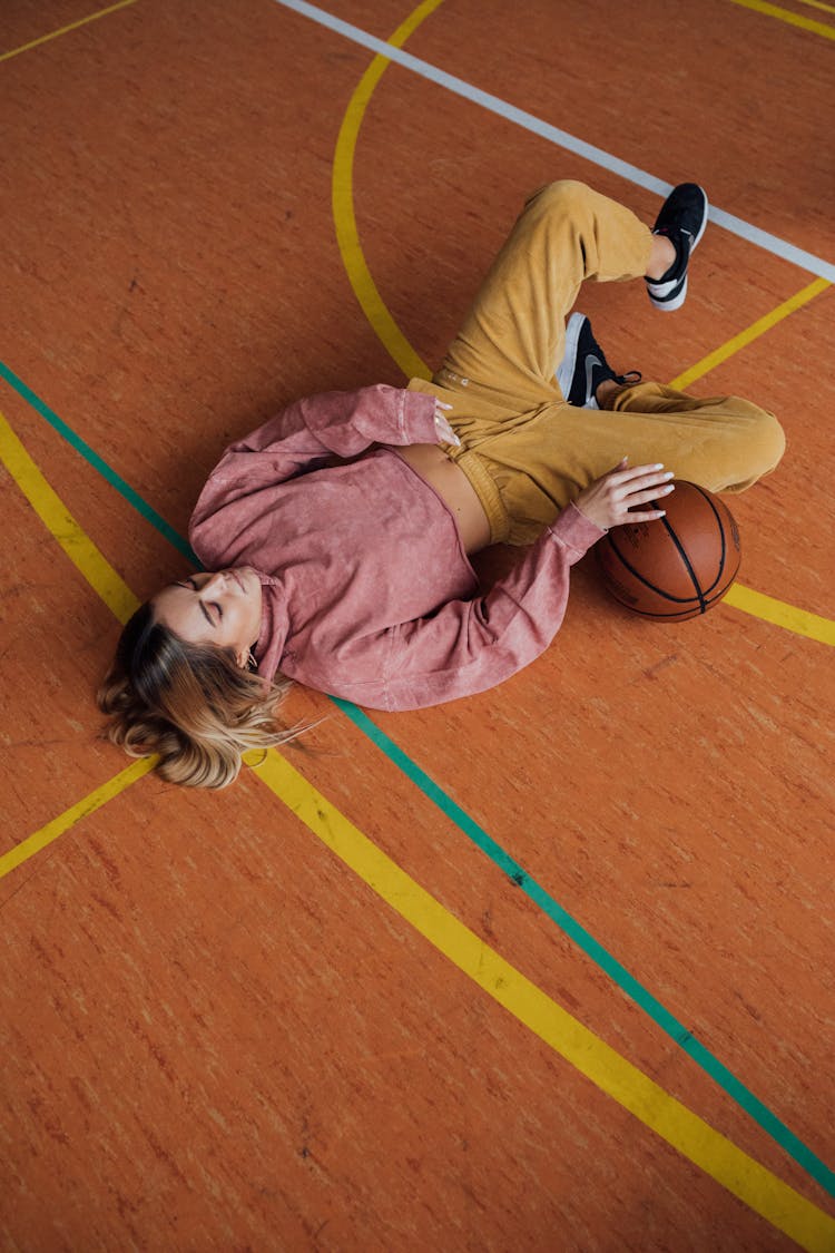 Woman In Pink Sweater Laying Down On A Basketball Court 