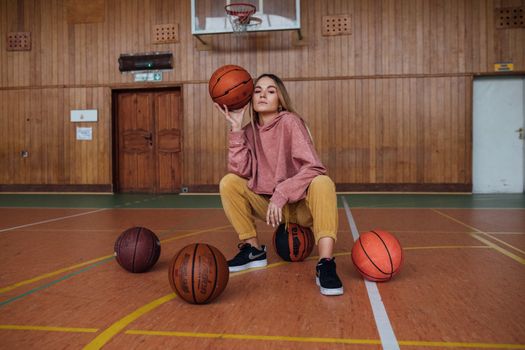 Stylish woman posing confidently with basketballs in an indoor court setting.