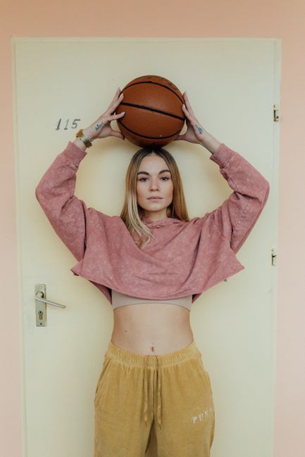 Fashion photoshoot of a woman with a basketball against a pastel background.