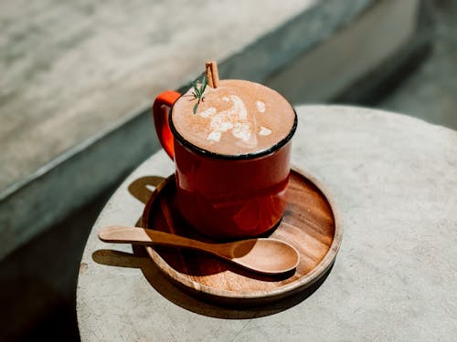 Free From above of delicious coffee with cinnamon and rosemary on wooden plate with spoon placed on wooden table in sunlight Stock Photo