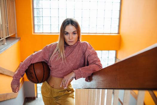 Young woman with basketball on colorful indoor staircase. Athletic portrait.
