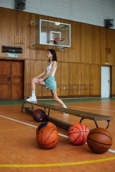 Young woman in gym attire stretching on a wooden bench in a gymnasium.