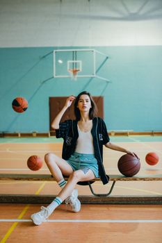 Woman in a sports hall sitting with basketballs around her, showcasing athletic fashion.