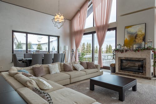 Comfortable lounge zone with soft furniture against fireplace near huge windows in villa