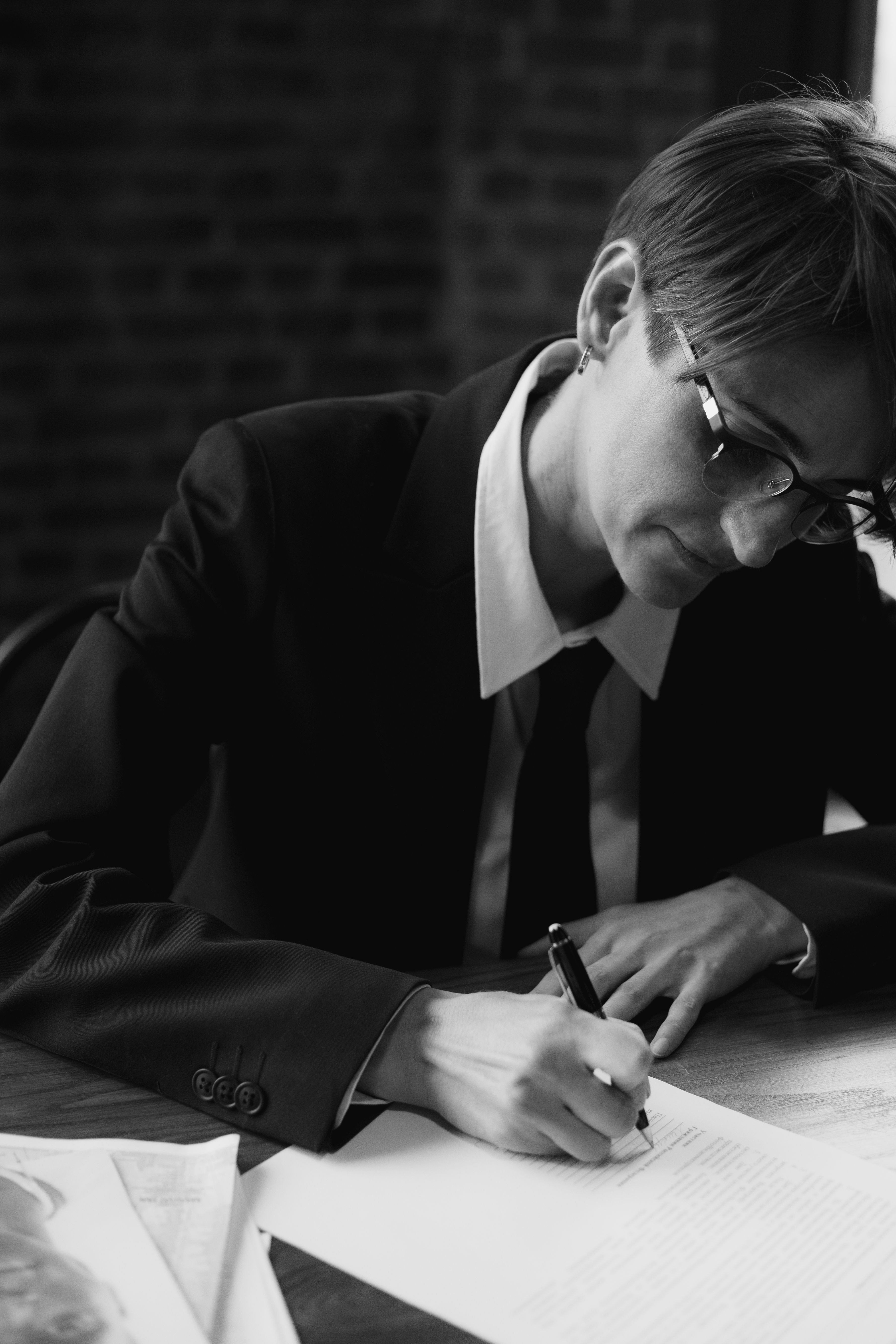 Businessperson in a suit writing notes indoors, enhanced by monochrome tones.
