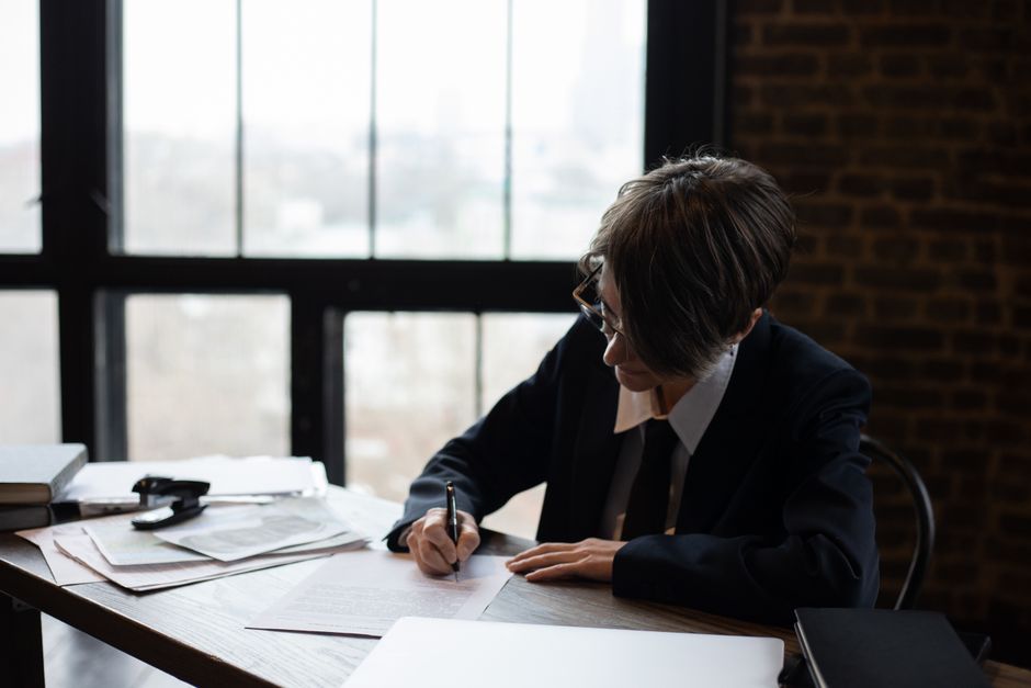 Profesional de negocios con traje formal escribiendo en un escritorio en un entorno de oficina con grandes ventanas.