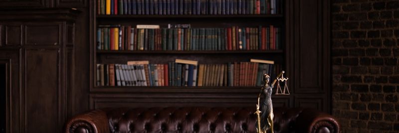 A classic study room with shelves of books, a gavel, and Lady Justice figurine on a green table.