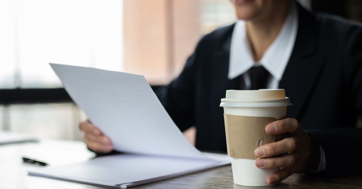 Focused businesswoman examining documents with a disposable coffee cup on a wooden desk. - Evidence evidence guide for caffeine performance systematic review