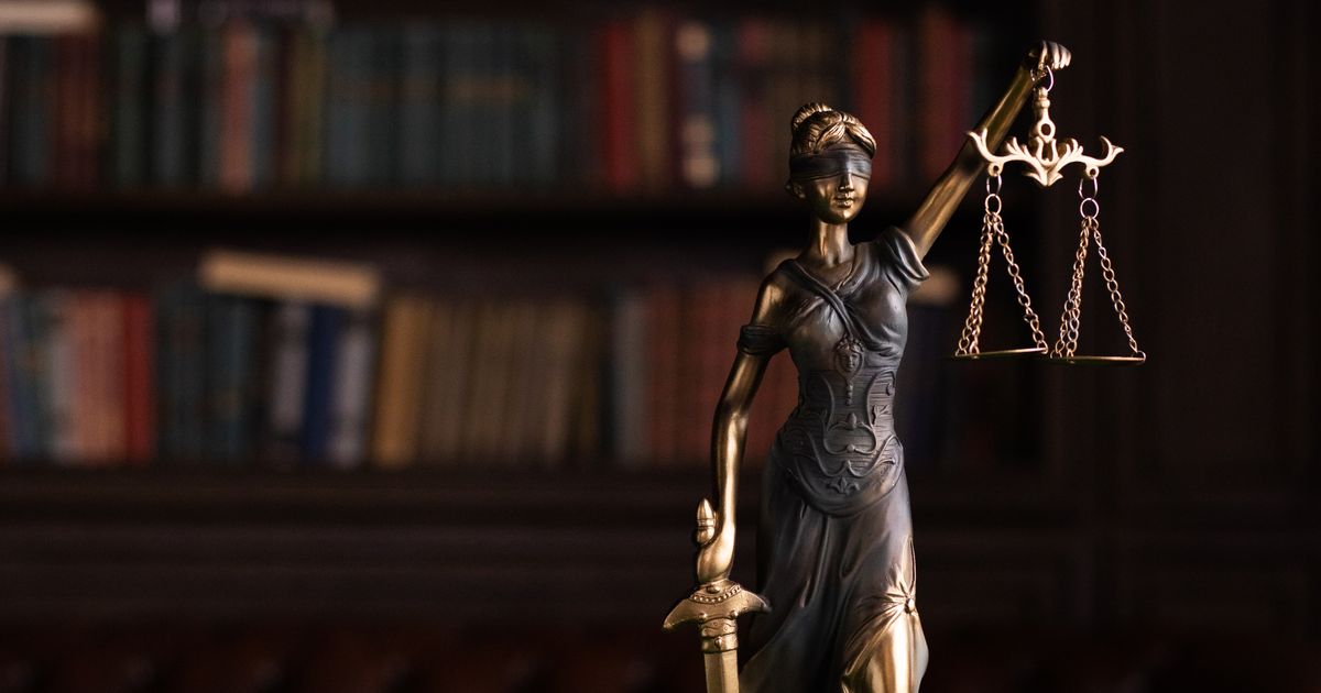 A Lady Justice statue and a gavel on a table in a law library.