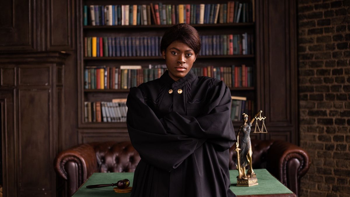 A confident female judge in a formal robe posing in a classic legal library setting.