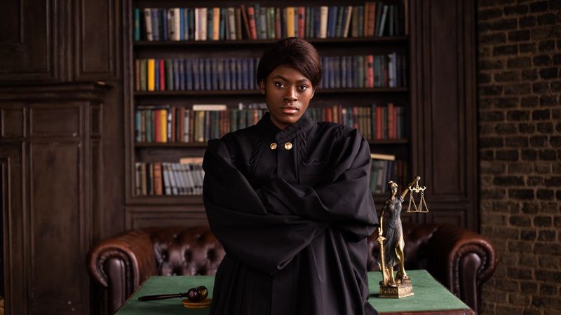 A confident female judge in a formal robe posing in a classic legal library setting.