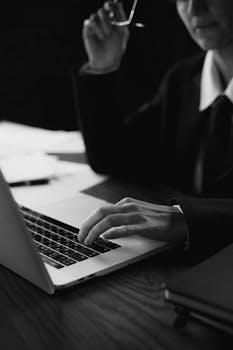 Black and white image of a person typing on a laptop, creating a focused work environment.
