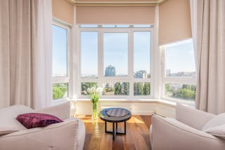 Interior of modern penthouse with comfortable white armchairs and round side table placed near windows overlooking city in sunny day