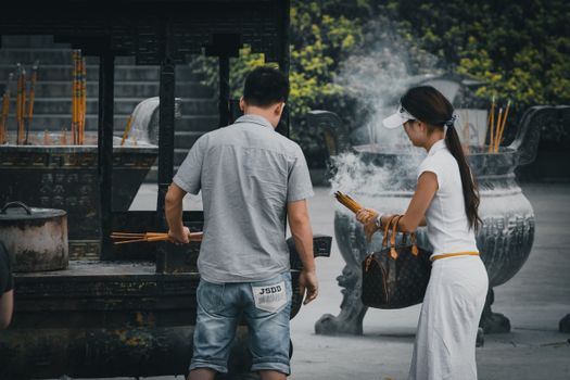 Unrecognizable Asian woman and man near incense burner outdoors