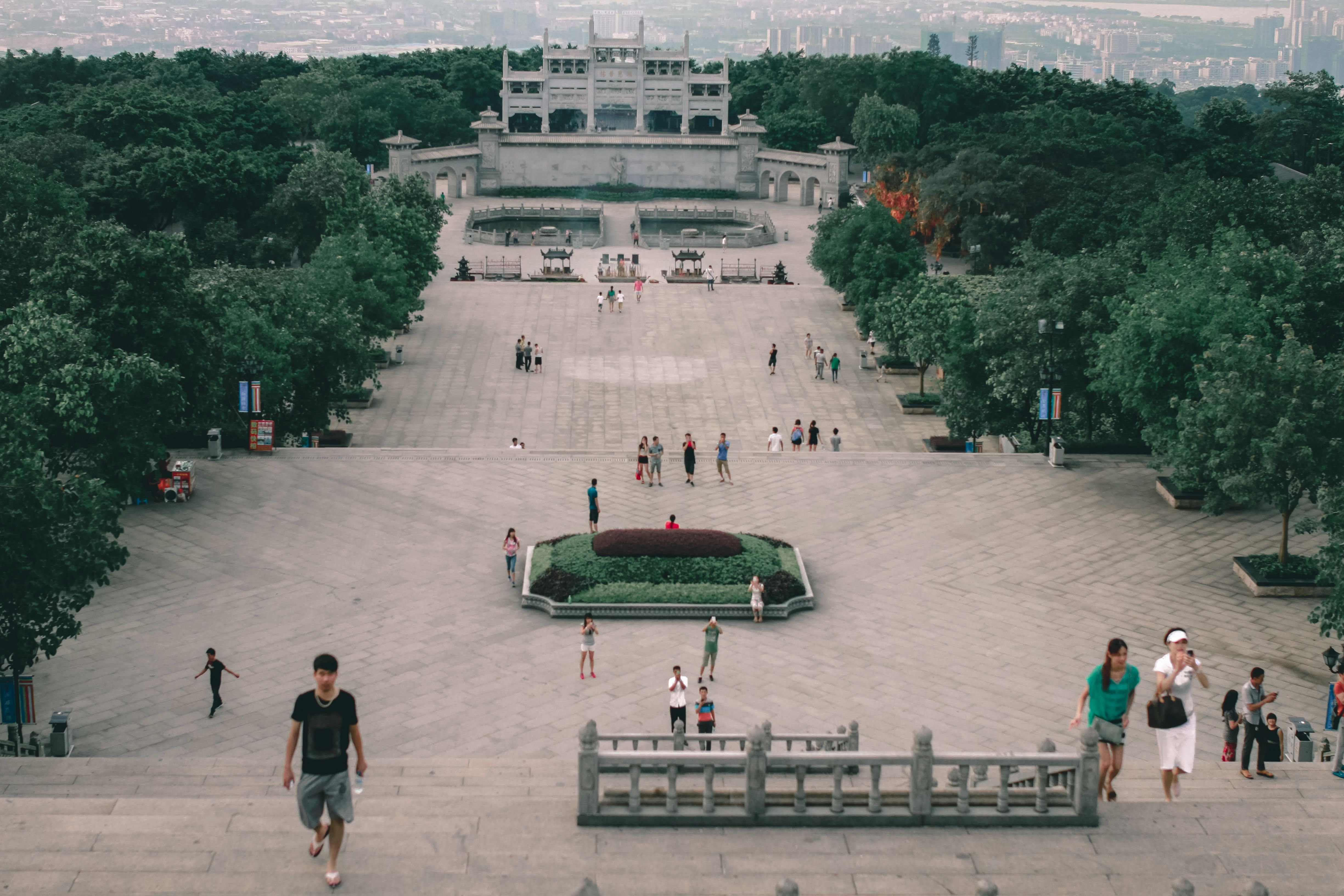 From above of anonymous ethnic travelers strolling on staircase against old stone construction and lush trees in town