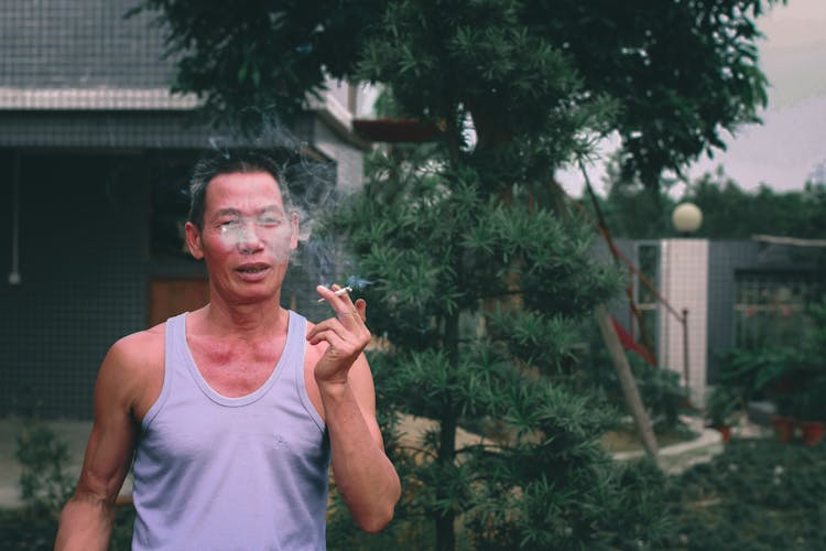 Mature Asian Man Smoking Cigarette In Garden