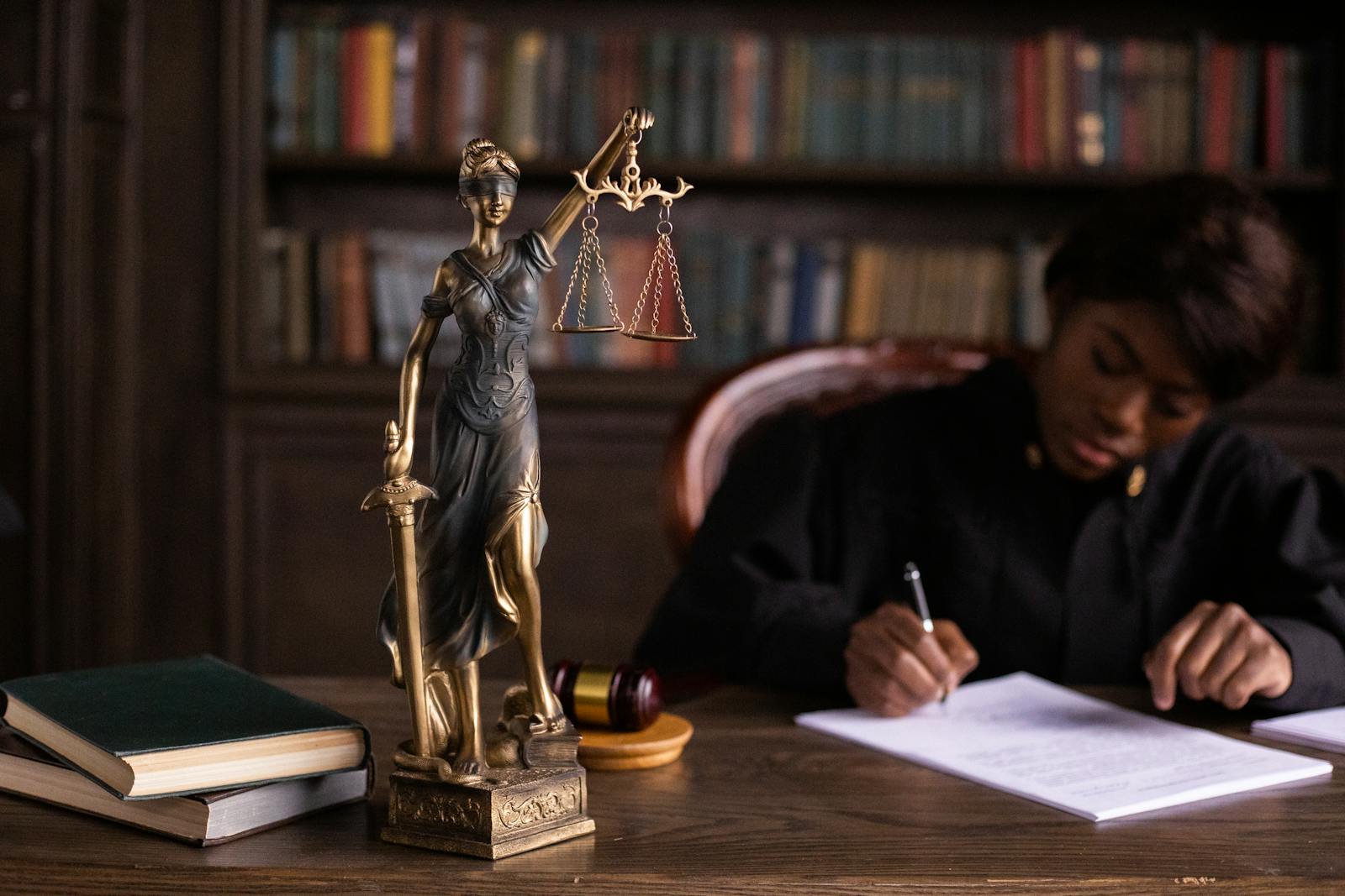 Judge writing on legal documents beside a Lady Justice statue