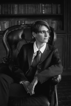 A sophisticated woman in formal attire seated in a classic library. Black and white portrait.