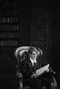 A Grayscale of a Woman in a Suit Reading Documents while Sitting on a Chair