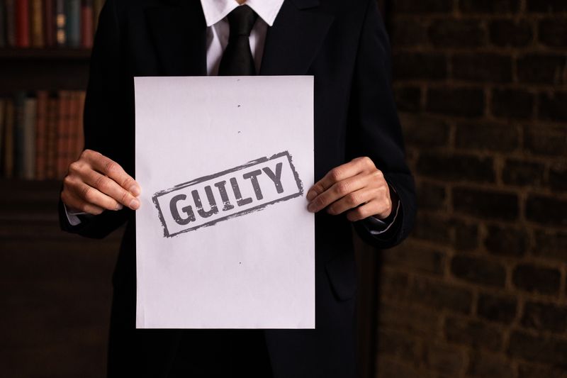 Hombre de negocios en traje formal sosteniendo un cartel con la palabra 'CULPABLE'.