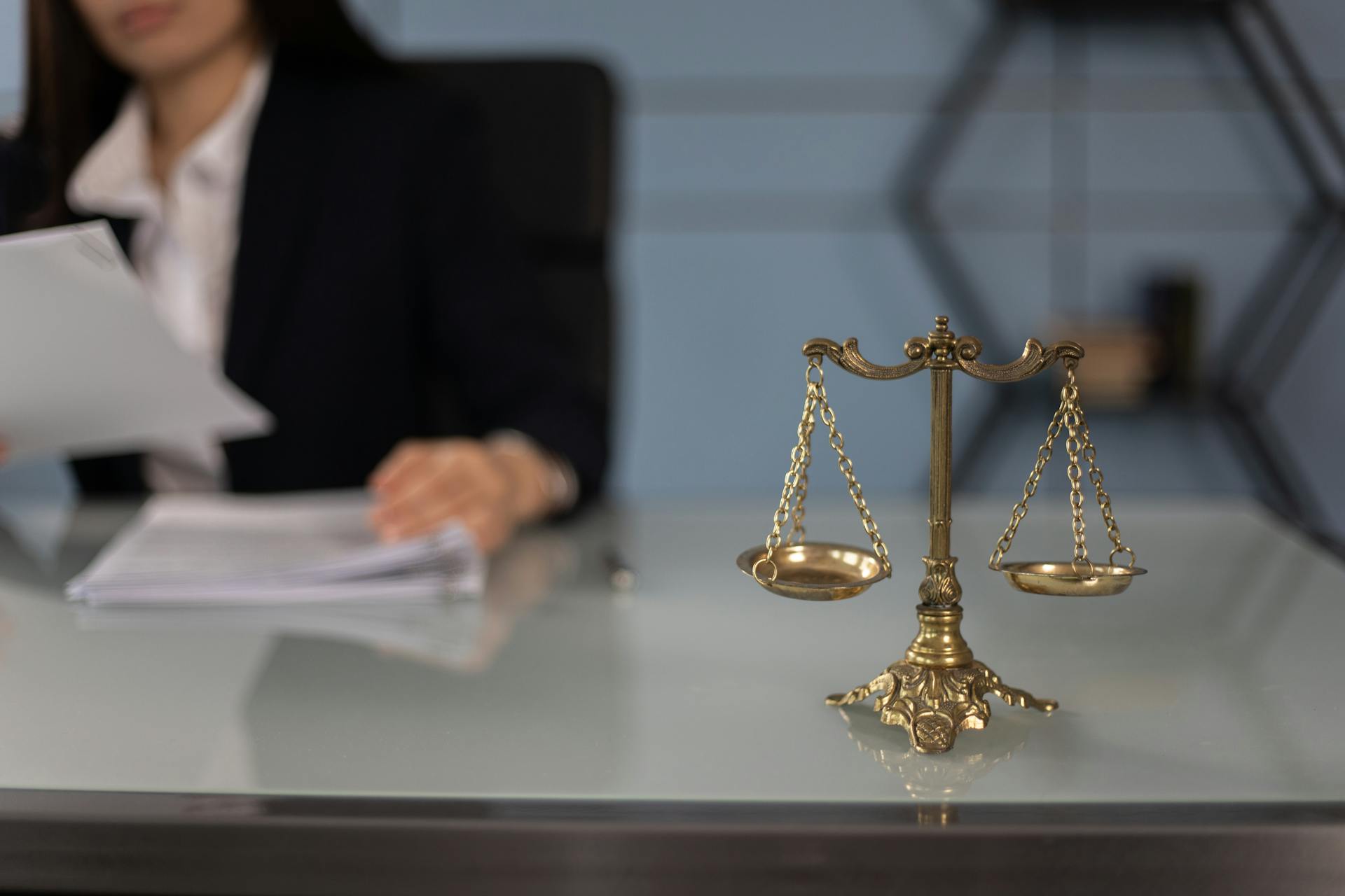 Balance scales on a desk in a professional office with a blurred businesswoman in the background.