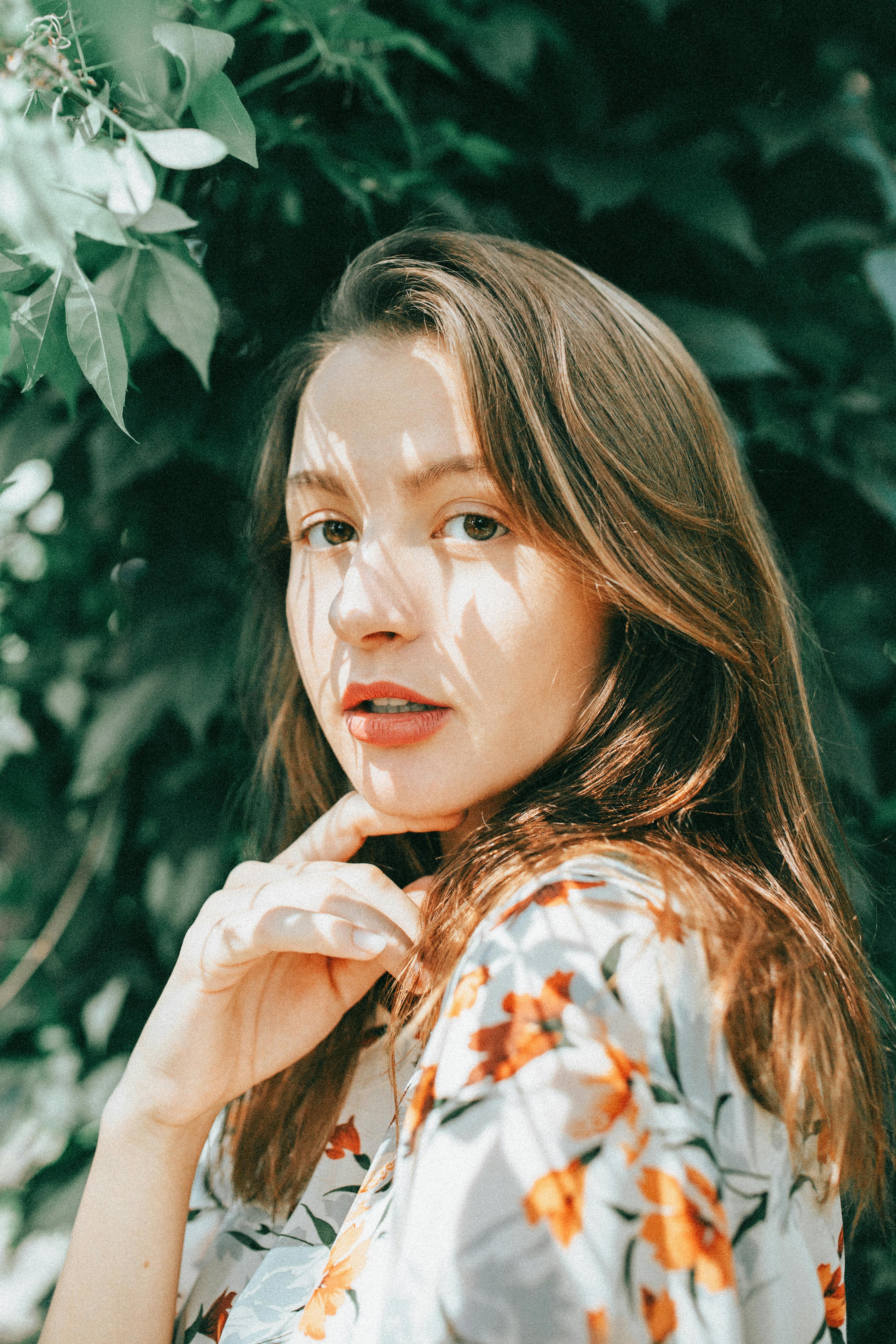 Portrait of a woman with long hair in natural light surrounded by foliage.