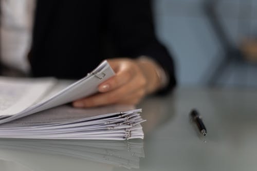 Free Close-Up Shot of a Person Holding a Paperwork Beside a Pen Stock Photo