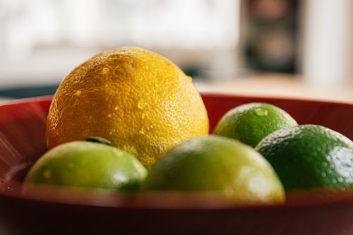 Free Close-up of fresh lemons and limes in a red bowl with a blurred background. Stock Photo