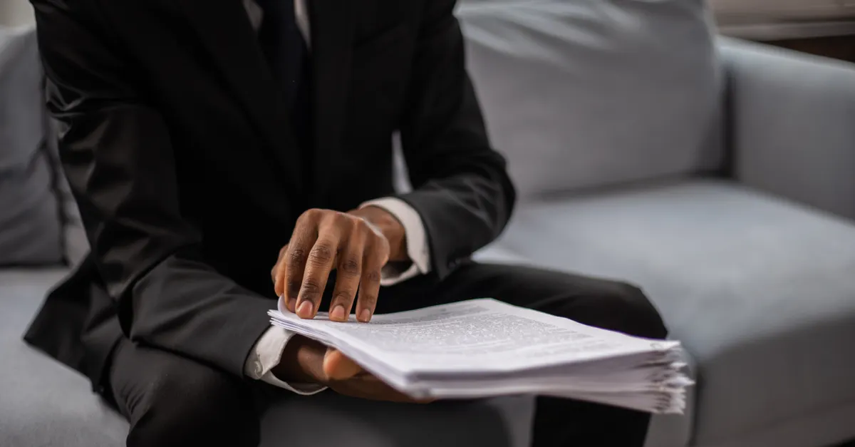 A lawyer at a desk surrounded by tall stacks of paper case files, the daily reality of reading long judgments.