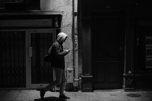Free Black and white of side view of anonymous person using smartphone and walking on street in residential district in evening Stock Photo