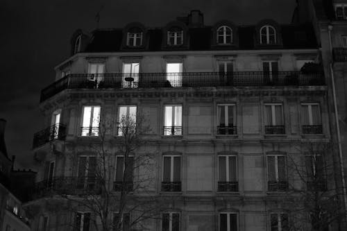 Black and white of exterior residential building with illuminated windows placed in city in evening time