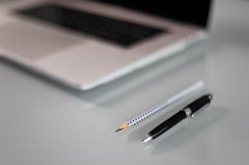 Close-Up Shot of a Pen and Pencil beside a Laptop 