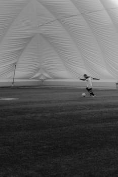 Black and white image of a soccer player in mid-action inside a sports dome.
