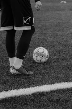 Black and white image of a soccer player preparing to kick the ball on a grass field.