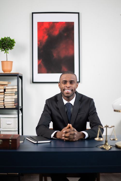 Free African American businessman smiling in an office environment, seated at a desk. Stock Photo