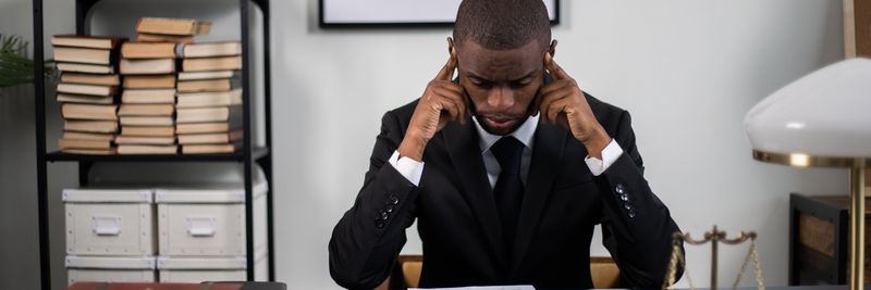 Businessman in suit reading documents at office desk, appearing stressed or thoughtful.