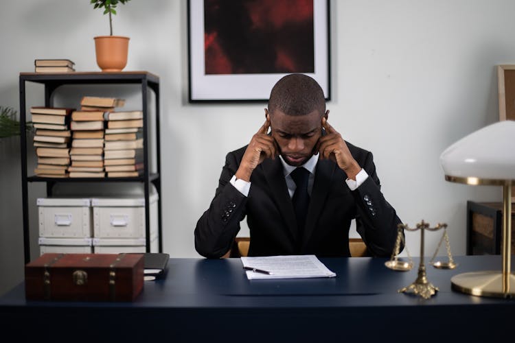 A Man In A Suit Reading A Document In His Office