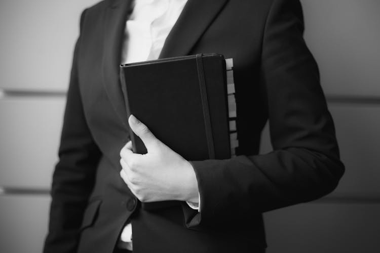 A Grayscale Of A Woman In A Suit Holding A Planner With Label Tabs