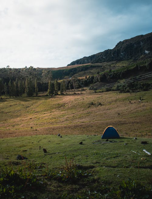 Blue Dome Tent on Green Grass Field Near Mountain Under White Clouds