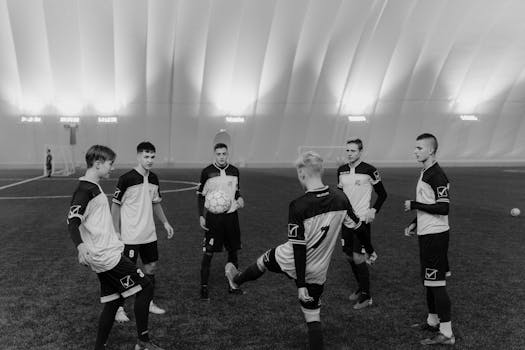 A group of male soccer players practicing indoors on an artificial field in monochrome.